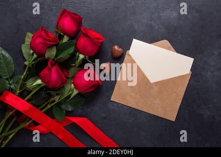 Bouquet de fleurs roses rouges, enveloppe, bonbons au chocolat sur fond de pierre noire carte de vœux de Saint-Valentin espace de copie plat Banque D'Images