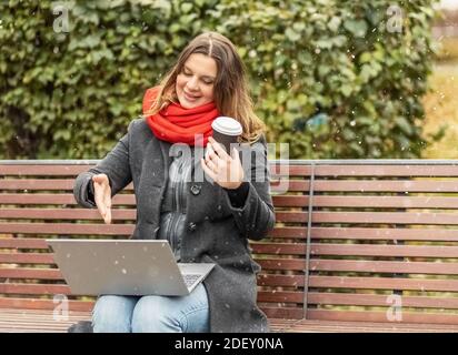 Jeune femme travaillant sur un ordinateur portable assis sur un banc de parc avec du café. Utilisation d'ordinateurs et d'achats en ligne. Formation à distance, formation en ligne Banque D'Images