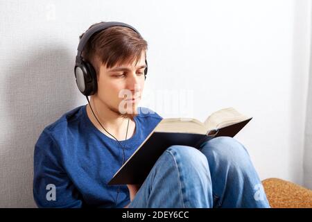 Un jeune homme dans un casque lit un livre à la maison Banque D'Images