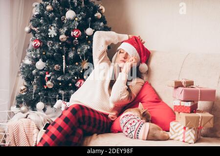 Femme endormie et fatiguée de l'emballage cadeau avec chien chiot sur un canapé dans le salon avec arbre de Noël à la maison. Banque D'Images