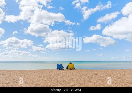 Un couple confortablement assis dans des chaises de plage bénéficiant d'une vue tranquille sur les eaux calmes et calmes de la mer. Banque D'Images