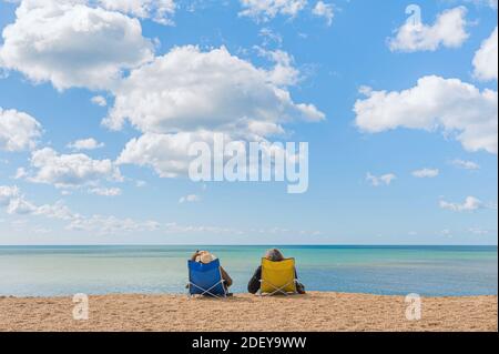 Un couple confortablement assis dans des chaises de plage bénéficiant d'une vue tranquille sur les eaux calmes et calmes de la mer. Banque D'Images