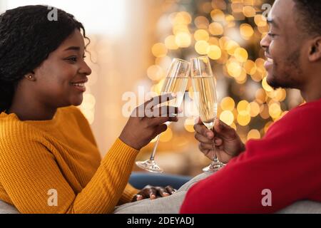 Un jeune couple afro-américain souriant clink des verres avec champagne à l'intérieur séjour Banque D'Images