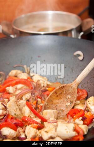 Une cuillère en bois mélangeant les tranches de poulet dans une casserole en métal avec poivrons et autres ingrédients Banque D'Images