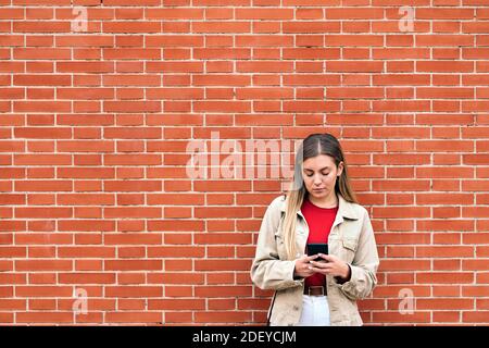 Photo de la fille blonde en utilisant son téléphone contre le mur rouge. Banque D'Images