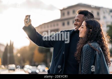 Photo de couple interracial d'amoureux prenant des photos avec le téléphone mobile dans la rue. Banque D'Images