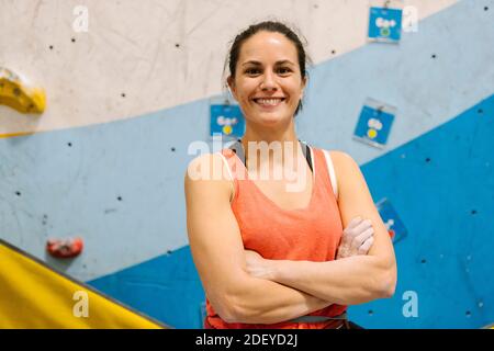 Photo d'une femme adulte debout devant un mur d'escalade et regardant la caméra. Elle porte un débardeur rouge et un pantalon bleu. Banque D'Images