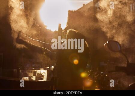 Photo d'un couple dans leurs années 30. Ils s'embrasent et prennent un selfie.le soleil se couche derrière eux. Ils portent un tissu décontracté. Banque D'Images