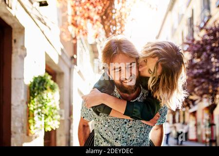 Photo d'un couple dans leurs années 30. La femme est sur le dos des ans. Elle l'embrasse. Ils portent des vêtements décontractés. Banque D'Images