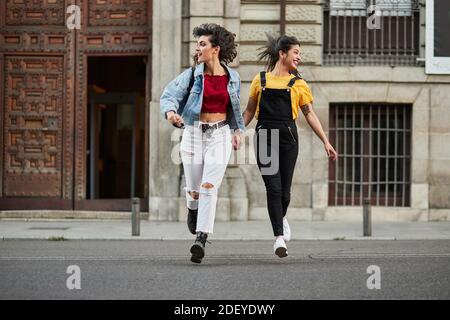 Photo de stock de deux adolescentes qui descendent dans la rue et tiennent les mains. Ils portent un tissu décontracté et des lunettes de soleil. Banque D'Images