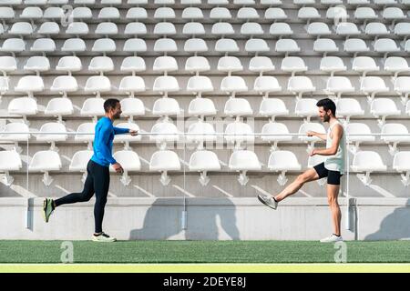 Photo d'athlètes blancs et noirs de sexe masculin qui se réchauffent avant de s'entraîner sur une piste athlétique. Ils sourient. Banque D'Images