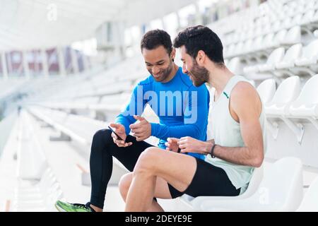 Photo de deux athlètes amis prenant une pause en utilisant le téléphone dans les gradins d'une piste sportive. Banque D'Images