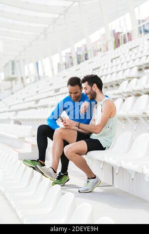 Photo de deux athlètes amis prenant une pause en utilisant le téléphone dans les gradins d'une piste sportive. Banque D'Images