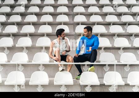 Photo de deux athlètes amis prenant une pause ayant une conversation dans les gradins d'une piste athlétique. Banque D'Images