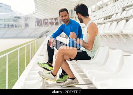 Photo de deux athlètes amis prenant une pause ayant une conversation dans les gradins d'une piste athlétique. Banque D'Images