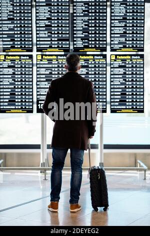 Photo d'un homme d'affaires méconnu qui regarde l'horaire des départs à l'aéroport. Il a une valise. Il porte des vêtements décontractés. Banque D'Images