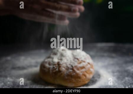 Concept de pain de cuisson flou, éclaboussure de farine avec les mains sur pain tradicional, arrière-plan sombre Banque D'Images