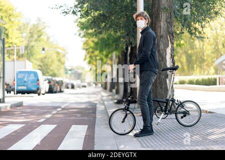 Photo de l'homme beau portant un masque facial avec son vélo amovible dans la rue. Banque D'Images
