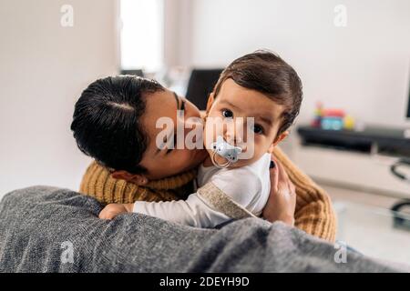 Photo de la jeune mère embrassant son petit bébé dans le canapé. Banque D'Images
