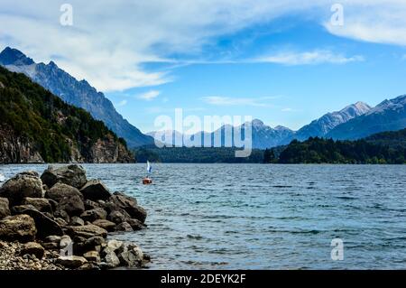 Rive du lac avec rochers, montagnes et pins. Un bateau à moteur flottant près d'une bouée. Été à Bariloche. Banque D'Images