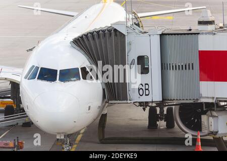 Vue avant d'un avion de type Airbus a320 sur le tablier de l'aéroport. Pont à jet et courroie de convoyeur à bagages connectés. Pilote derrière le pare-brise. Banque D'Images