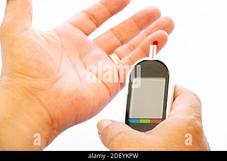 Homme faisant un test de glucose avec une goutte de sang sur un appareil de diabète sur un fond blanc. Banque D'Images