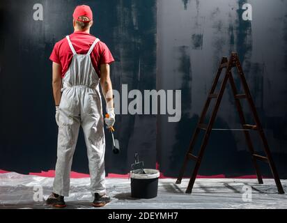 Homme peint un mur. Peintre en rouge mur de peinture en noir Banque D'Images