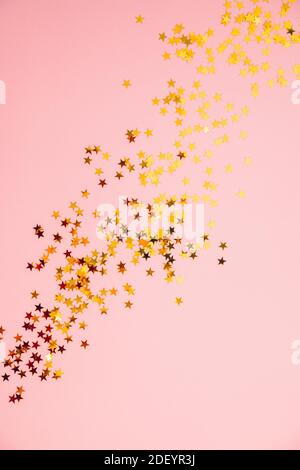 Des étincelles dorées d'étoiles éparpillées au hasard sur fond rose, sur fond plat festif. Mise au point sélective. Banque D'Images