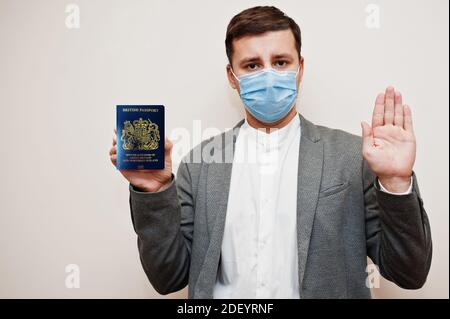 Homme européen en tenue officielle et masque facial, montrer passeport Royaume-Uni avec main stop signe. Confinement du coronavirus en Europe concept de pays. Banque D'Images