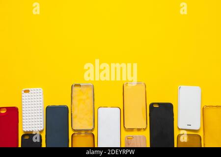 Pile de couvercles arrière en plastique multicolore pour téléphone mobile. Choix d'accessoires de protection pour smartphone fond. Téléphone en silicone sur fond jaune Banque D'Images