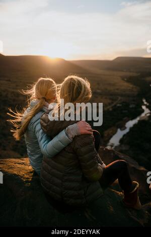 Mère et fille regardant le coucher du soleil assis sur le sommet de montagne luxuriant Banque D'Images