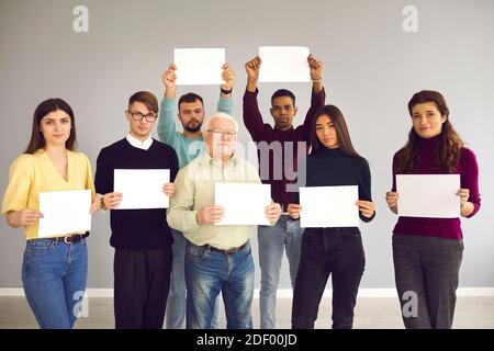 Groupe de personnes différentes debout ensemble, tenant des feuilles de papier blanches et regardant l'appareil photo Banque D'Images
