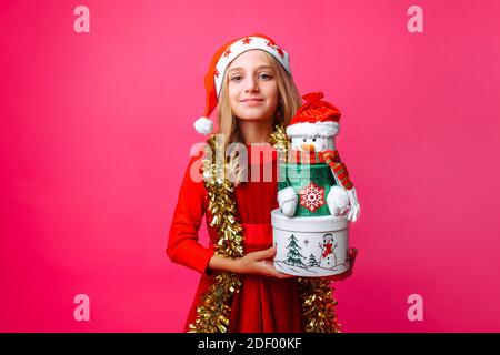 Adolescente portant un chapeau de père Noël et une guirlande sur le cou tenant des boîtes cadeaux de Noël, sur fond rouge Banque D'Images