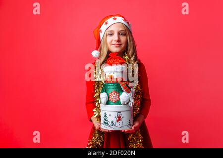 Adolescente portant un chapeau de père Noël et une guirlande sur le cou tenant des boîtes cadeaux de Noël, sur fond rouge Banque D'Images