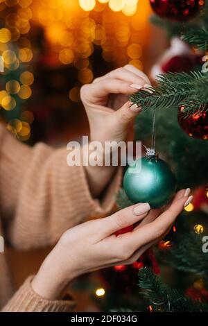 Gros plan des mains d'une femme méconnaissable décorant des boules colorées d'arbre de Noël dans un salon confortable. Banque D'Images