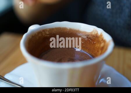 Une tasse de porcelaine blanche de chocolat chaud ou de cacao sur une table en bois. Sur la soucoupe se trouve une cuillère et en arrière-plan vous pouvez voir un chandail bleu flou a Banque D'Images
