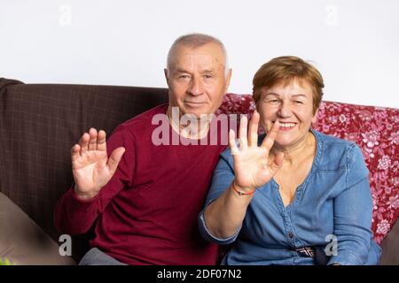 Portrait d'un couple âgé assis sur le canapé et en agitant les mains devant la caméra. Banque D'Images
