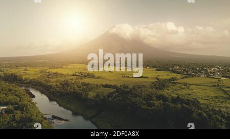 Le soleil tropique brille au-dessus de la rivière à l'éruption du volcan aérien. Champs, prairies à personne nature paysage. Vallée de l'herbe verte sur les rives du ruisseau tropical à la campagne des Philippines. Site cinématographique de Mayon Banque D'Images