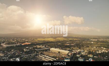 Le soleil brille au-dessus du volcan Mayon qui éclate à l'antenne de Legazpi Cityscape. Site phare épique des Philippines sur les routes et les bâtiments urbains. Vallée d'herbe verte du mont à flanc de colline. Nature cinématographique et ville tropicale Banque D'Images