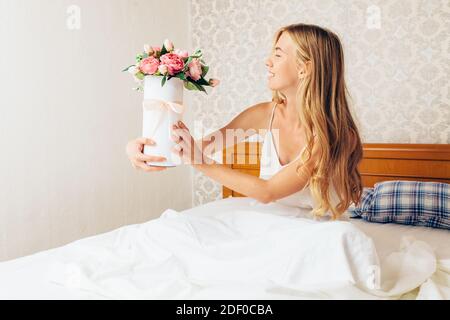 Jeune fille belle avec des fleurs de pivoine, assise sur le lit. Elle s'est réveillée et a reçu un bouquet de fleurs Banque D'Images