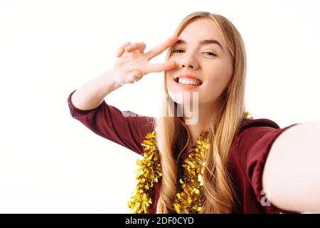 Portrait d'une fille joyeuse dans une robe rouge prenant une photo d'elle-même. Et montre deux doigts sur l'écran, isolés sur un fond blanc. CHR Banque D'Images