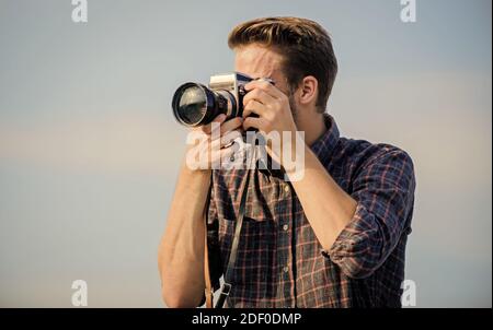 Reporter prend la photo. Paramètres manuels. Blogueur de voyage. Équipement vintage. Photographe Hipster. Blogger tournage vlog. Guy plein air bleu ciel fond. Beau blogger gars voyageur rétro appareil photo. Banque D'Images