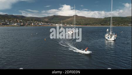 Yachts et bateau à moteur à la baie de la côte verte de l'île aérienne. Paysage de montagne à la ville de Brodick, île d'Arran, Écosse. Croisière d'été à bord de voiliers et de bateaux à moteur sur la côte verte de la colline Banque D'Images