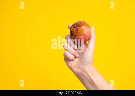 Une main femelle tient une pomme pourrie avec un ver sur fond jaune. Produits périmés. Banque D'Images