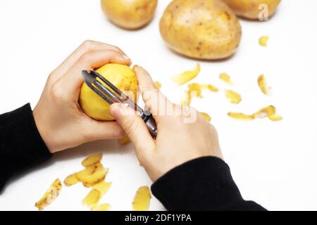 Mains d'un enfant épluchant une pomme de terre avec un éplucheur à la cuisine, aidant la main. Gros plan Banque D'Images