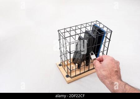 main ouvrant ou fermant la serrure sur une cage avec trois téléphones mobiles verrouillés dans une cage avec un cadenas, concept d'isolement social ou d'abus de téléphone et ainsi de suite Banque D'Images