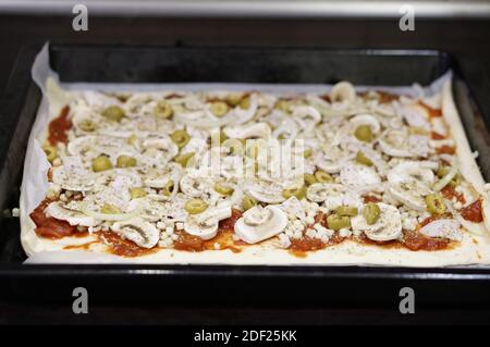 Photo d'une pizza rectangulaire brute surmontée d'une zone de mise au point douce avec des champignons et des olives dans une casserole Banque D'Images