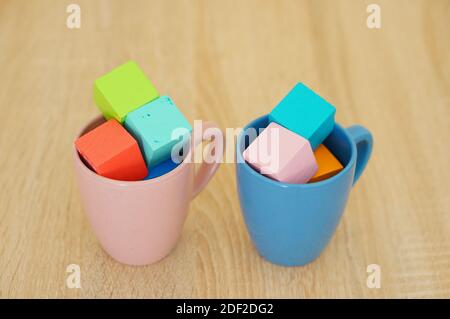 Petits cubes de différentes couleurs à l'intérieur des tasses roses et bleues Banque D'Images