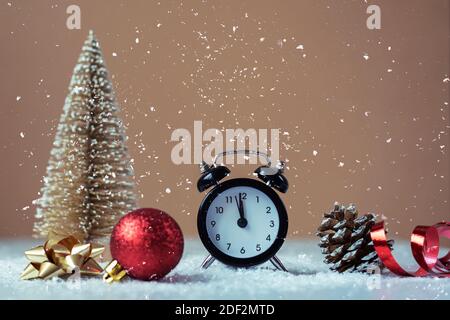 Réveil, jouet arbre de Noël et cône de pin sur fond beige avec neige tombant. Décorations de Noël, concept nouvel an. Gros plan. Banque D'Images