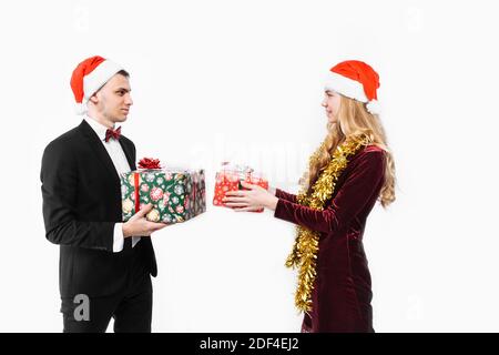 Un couple heureux d'amoureux en chapeaux de Père Noël se donnant les autres cadeaux de Noël. Sur fond blanc. Banque D'Images